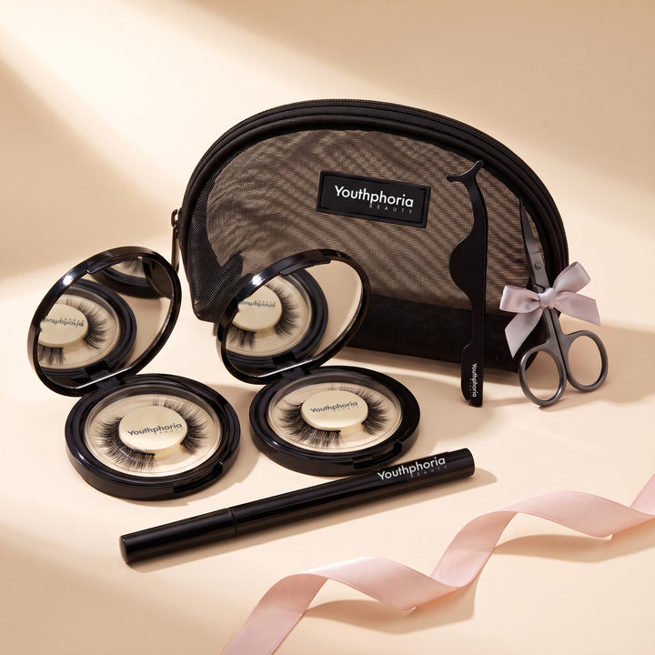 Youthphoria Ultimate Starter Kit laid out on a warm cream studio backdrop: two open magnetic lash compacts with lashes inside, the black magnetic eyeliner pen, the mesh makeup bag, the lash applicator and the lash scissors