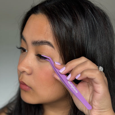 Woman using a purple brow brush with 'Youthphoria' branding. Demonstration on how to press and clamp down Youthphoria Press-on lashes
