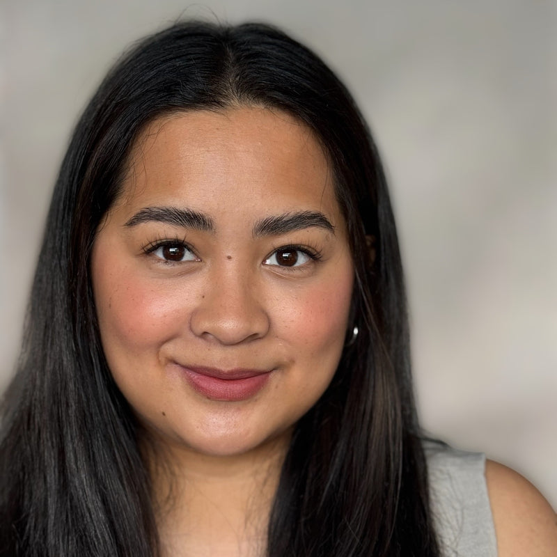 Woman with long dark hair smiling against a neutral background wearing wispy Youthphoria Fastbond Press-on lashes 