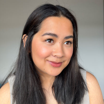 Woman with long dark hair smiling against a neutral background wearing wispy Youthphoria Fastbond Press-on lashes 